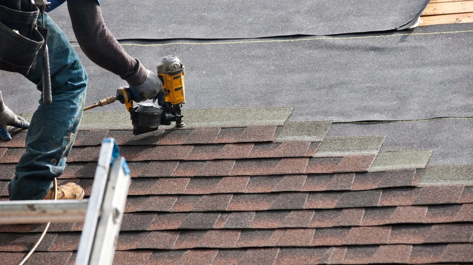 A roofer fastening asphalt shingles with a pneumatic coil nailer
